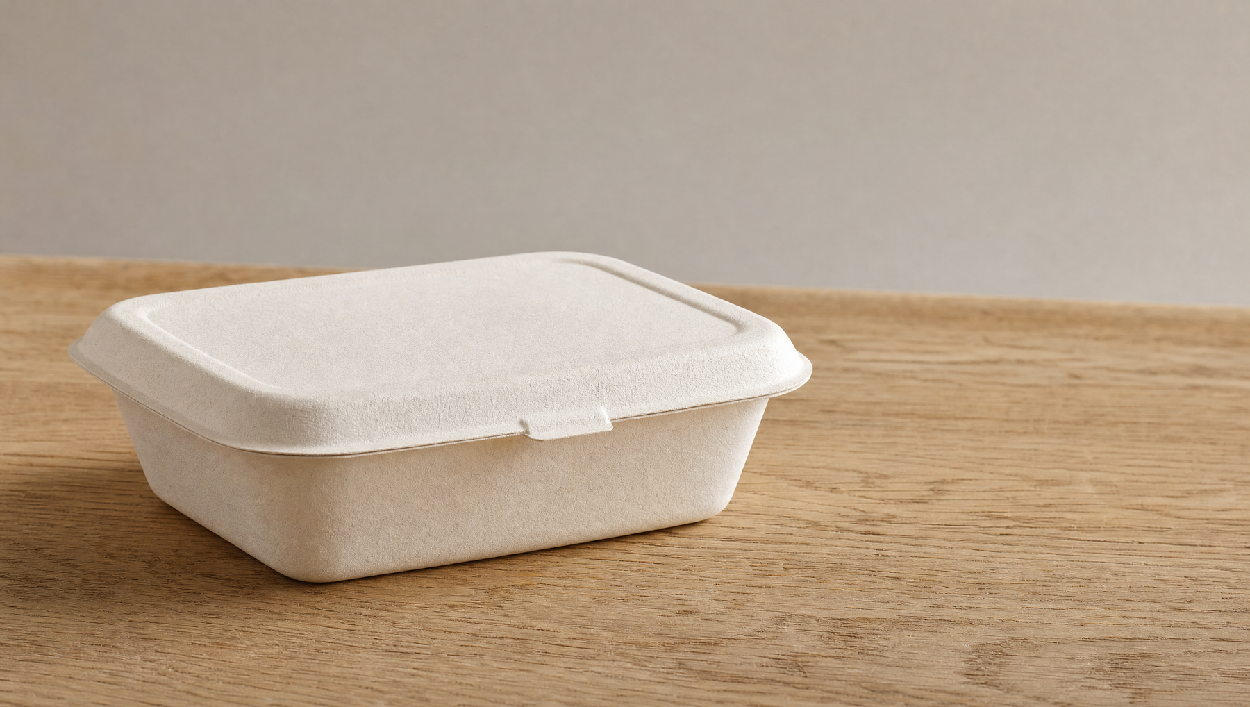 White sugarcane bagasse fibre food container on a light wood surface, soft natural daylight, PFAS-free moulded fibre packaging
