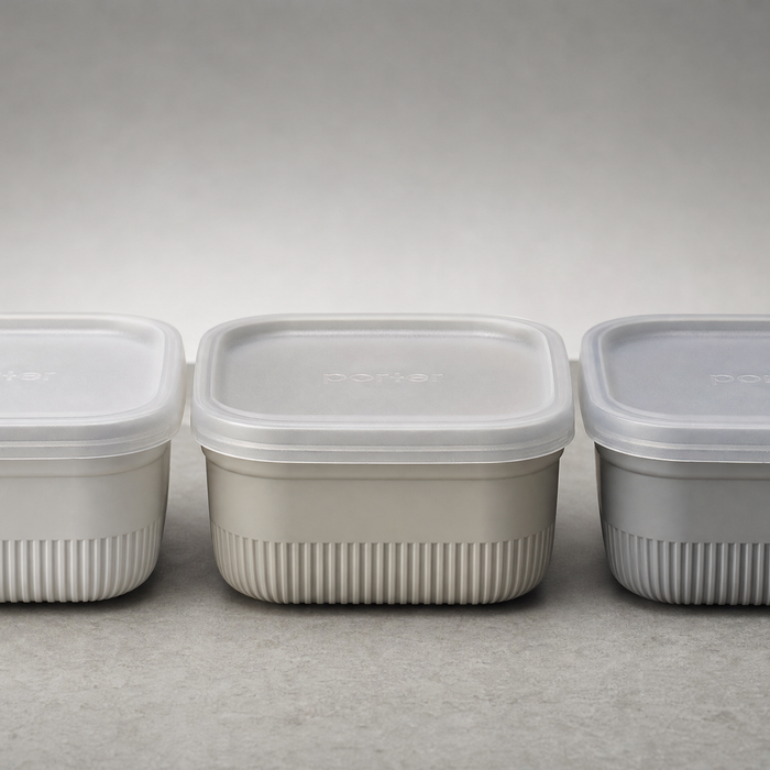 Three small food containers side by side on a neutral grey surface, soft daylight, compostable packaging comparison