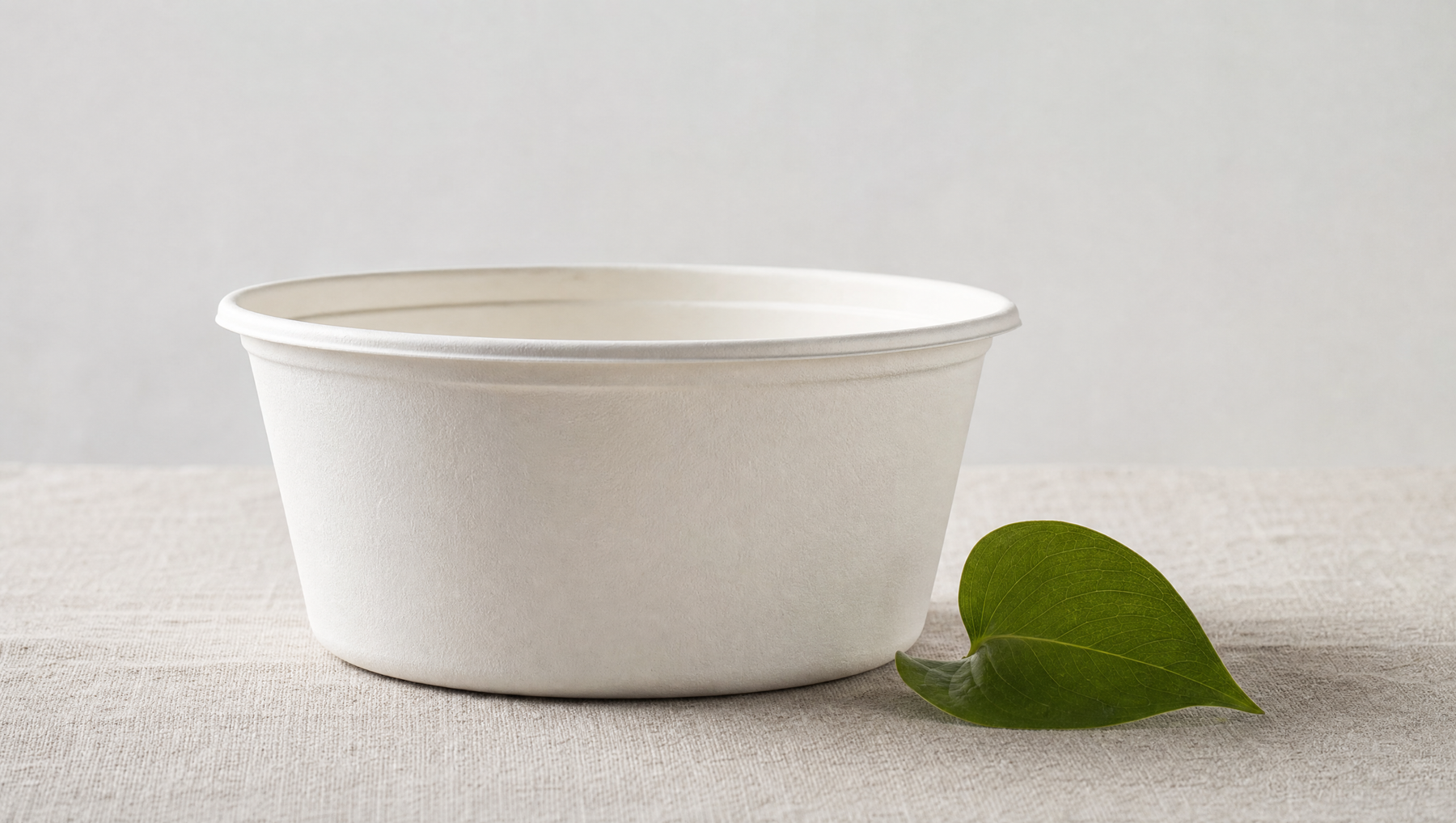 White compostable food container with a small green leaf next to it on neutral surface, sustainability claim compliance