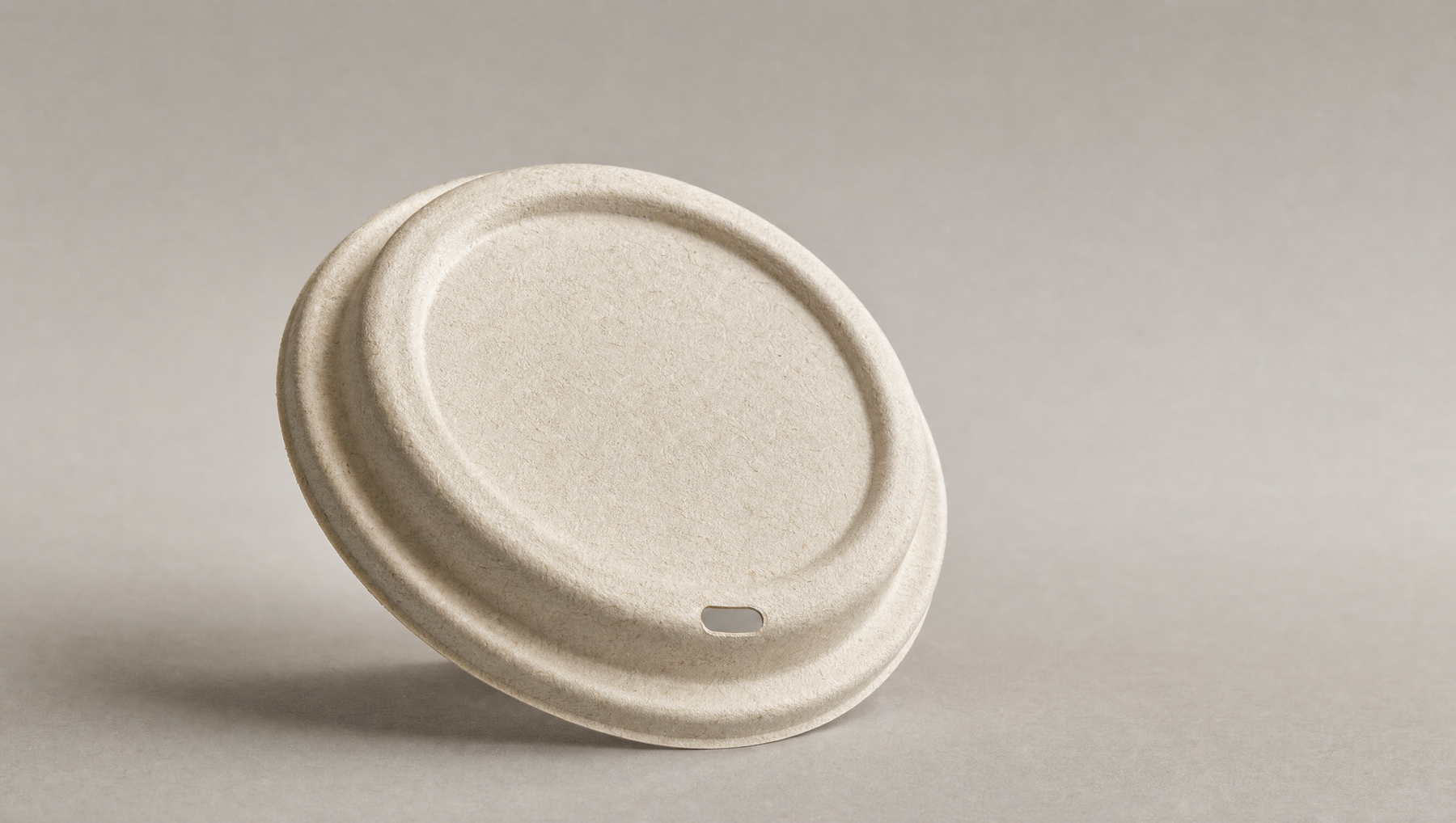 Compostable bagasse fibre coffee cup lid on neutral surface, product photography of PE PS and CPLA alternatives