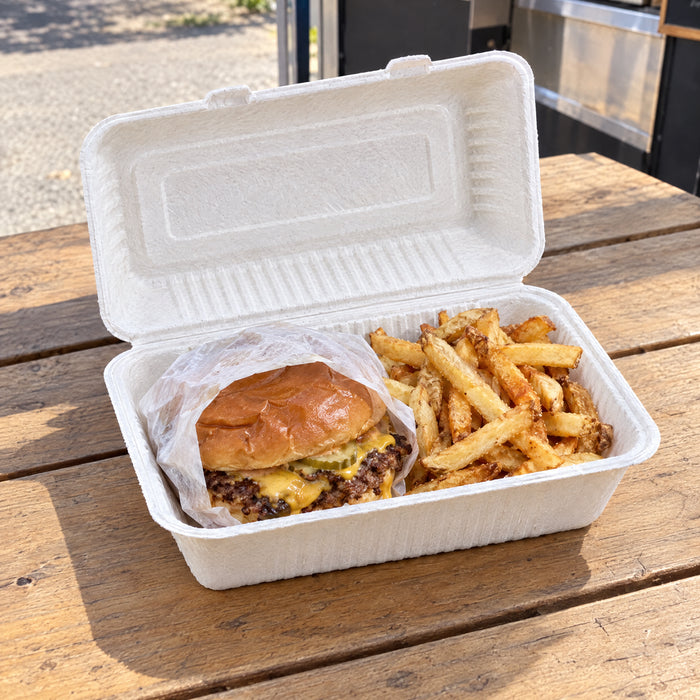 Smash burger and fries in a bagasse 9x6 clamshell on a wooden picnic table