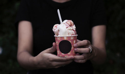 Printed paper ice cream cup filled with ice cream, held in two hands